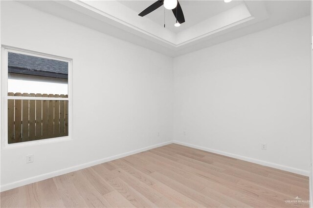 spare room featuring light wood-type flooring, a raised ceiling, and ceiling fan