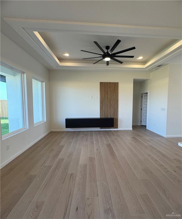 unfurnished room with a raised ceiling, light hardwood / wood-style flooring, and ceiling fan