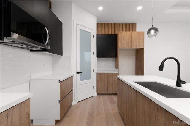 kitchen with decorative backsplash, light hardwood / wood-style flooring, hanging light fixtures, and sink