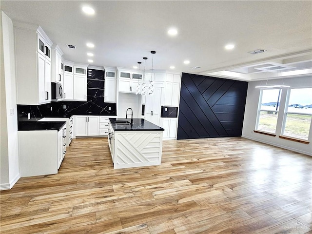 kitchen featuring sink, decorative light fixtures, a center island with sink, light hardwood / wood-style flooring, and white cabinetry