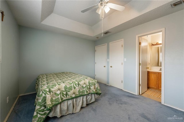 bedroom with carpet floors, a tray ceiling, ensuite bath, and visible vents