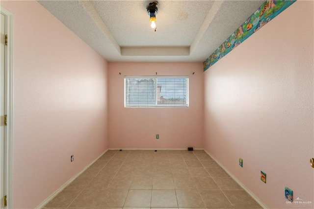 empty room with a textured ceiling, light tile patterned floors, a raised ceiling, and baseboards