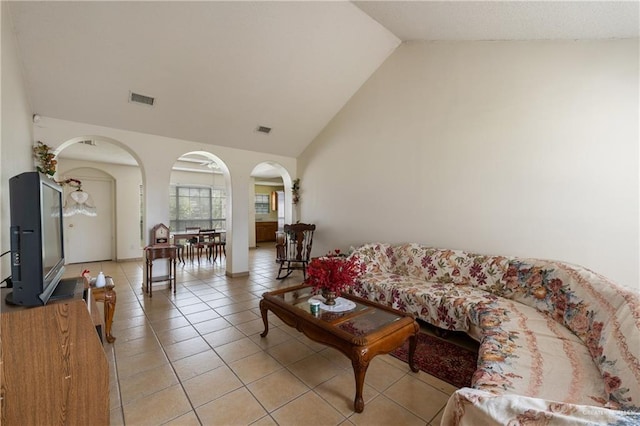 living area with light tile patterned floors, visible vents, arched walkways, and high vaulted ceiling