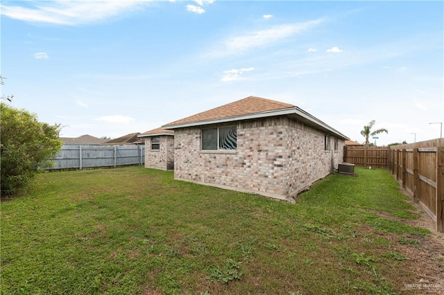 rear view of property with a fenced backyard, a yard, brick siding, and central AC unit