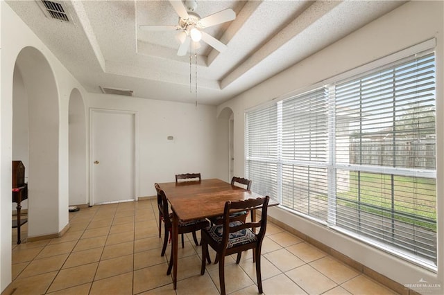 dining area with arched walkways, a raised ceiling, and light tile patterned flooring