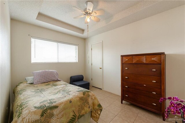 bedroom with light tile patterned floors, ceiling fan, a raised ceiling, and a textured ceiling