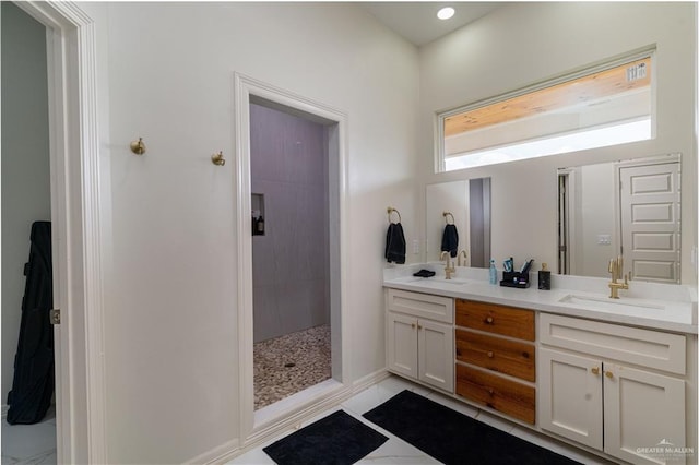 full bathroom featuring double vanity, a tile shower, tile patterned flooring, and baseboards