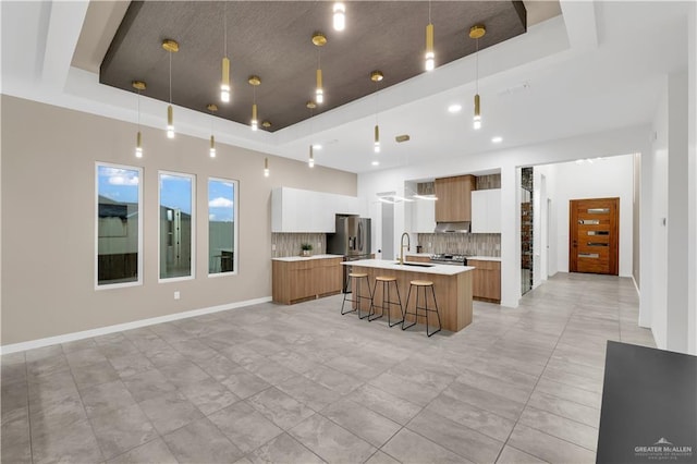 kitchen featuring a kitchen island with sink, a tray ceiling, and white cabinets