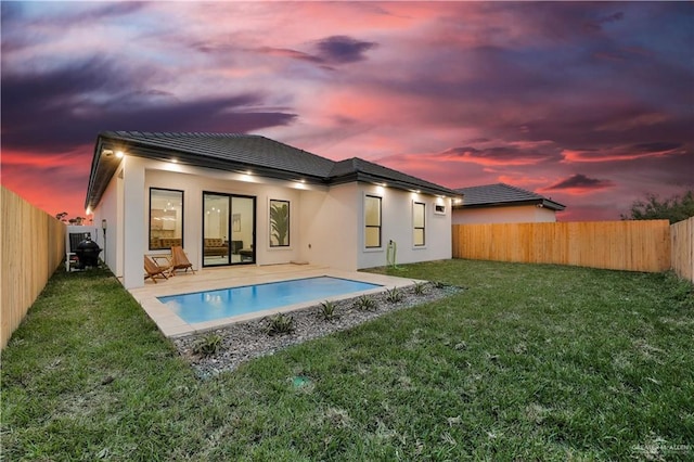 back house at dusk featuring a patio and a yard