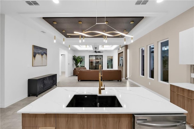 kitchen with light stone counters, stainless steel dishwasher, decorative light fixtures, and sink