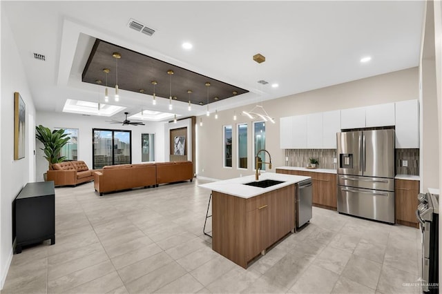 kitchen featuring stainless steel appliances, white cabinetry, a kitchen island with sink, and a tray ceiling