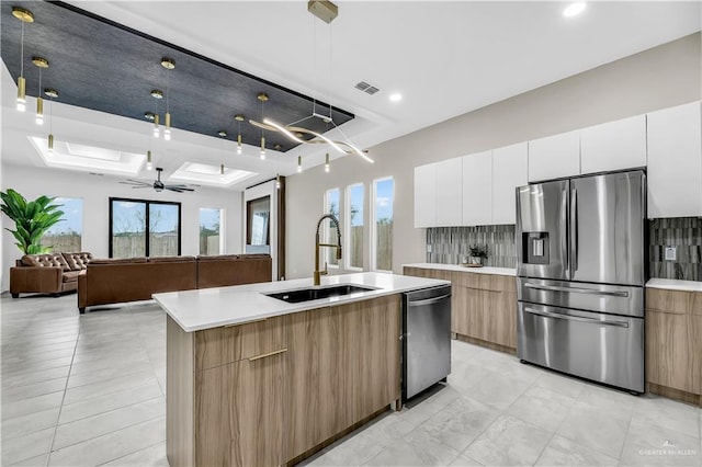 kitchen with sink, appliances with stainless steel finishes, white cabinets, a center island with sink, and decorative light fixtures