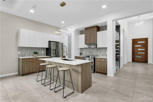 kitchen with white cabinetry, hanging light fixtures, stainless steel appliances, and an island with sink