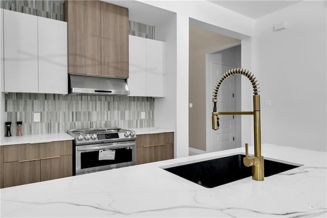 kitchen featuring sink, tasteful backsplash, light stone counters, white cabinets, and gas range