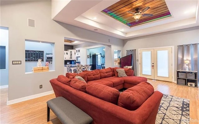 living room with light wood-style floors, a tray ceiling, and french doors