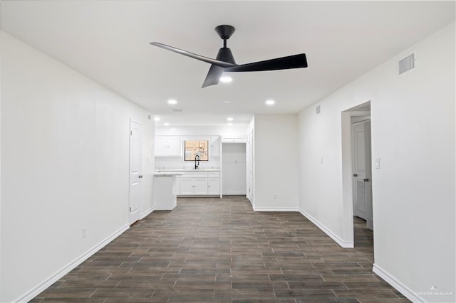 unfurnished living room with dark wood-style floors, baseboards, ceiling fan, and a sink