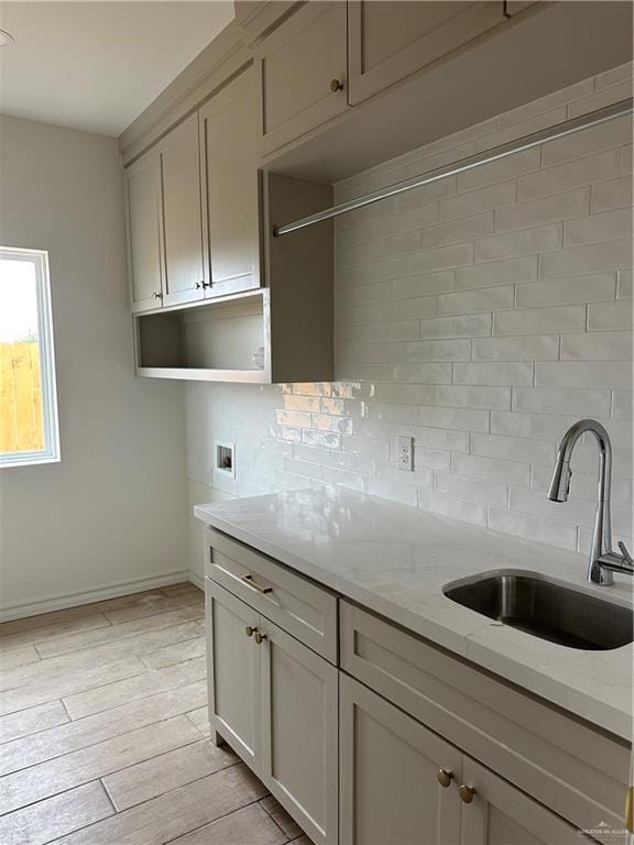 kitchen with baseboards, light wood-style flooring, backsplash, light stone countertops, and a sink