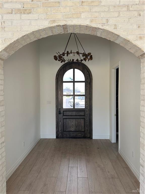 foyer with baseboards, arched walkways, and wood finished floors