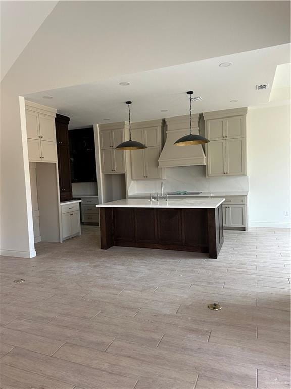 kitchen featuring visible vents, baseboards, light wood-style flooring, a kitchen island with sink, and custom exhaust hood