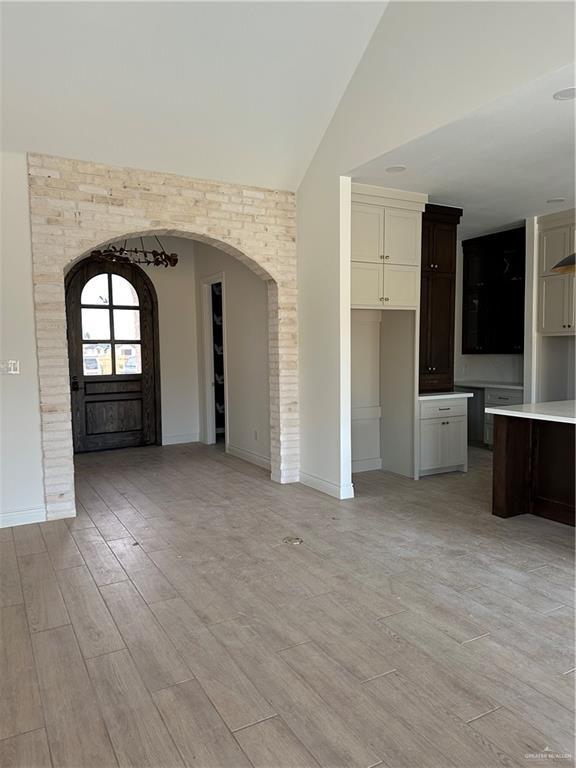 foyer featuring arched walkways, light wood finished floors, vaulted ceiling, and baseboards