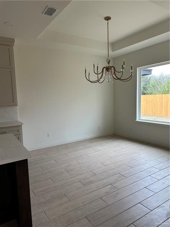 unfurnished dining area featuring light wood finished floors, a raised ceiling, visible vents, a chandelier, and baseboards