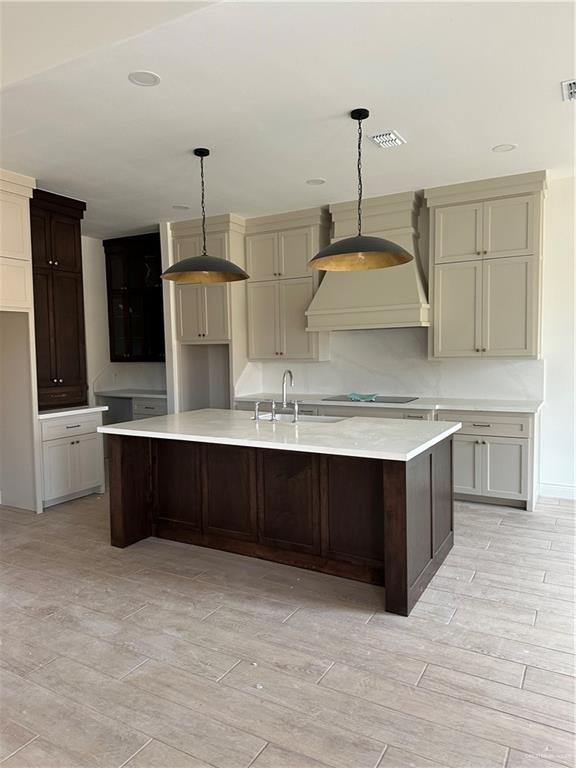 kitchen featuring a large island, black electric stovetop, wood finish floors, premium range hood, and a sink