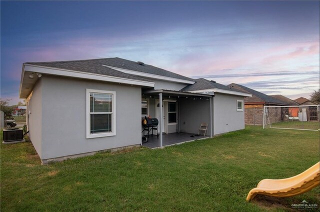 back house at dusk with a patio, a yard, and central AC