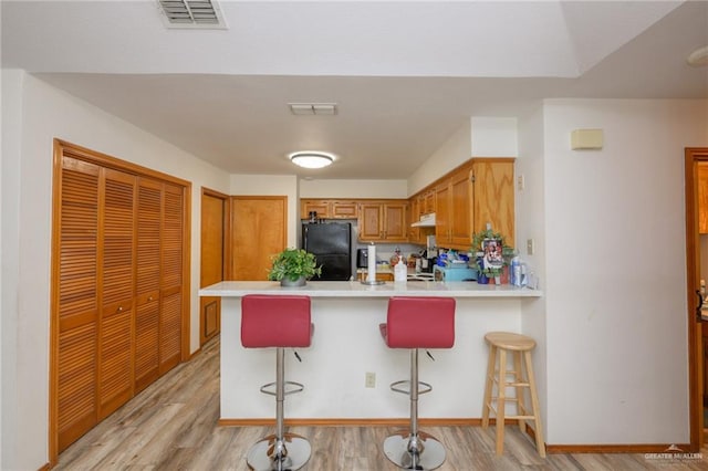 kitchen featuring a kitchen bar, light hardwood / wood-style floors, kitchen peninsula, and black refrigerator