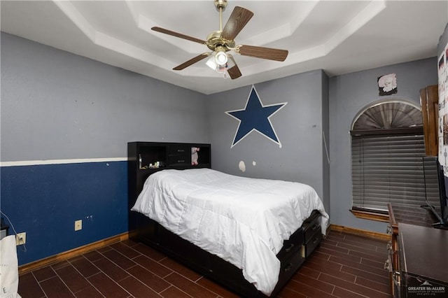 bedroom featuring baseboards, a raised ceiling, and wood finish floors