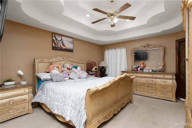 bedroom with a raised ceiling, a ceiling fan, and light colored carpet