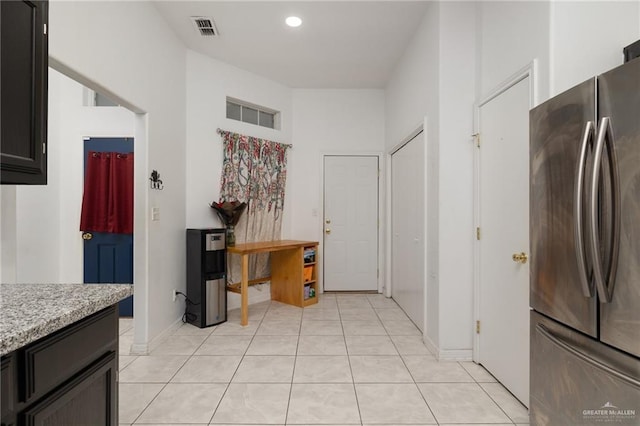 kitchen with stainless steel refrigerator, light stone countertops, and light tile patterned floors