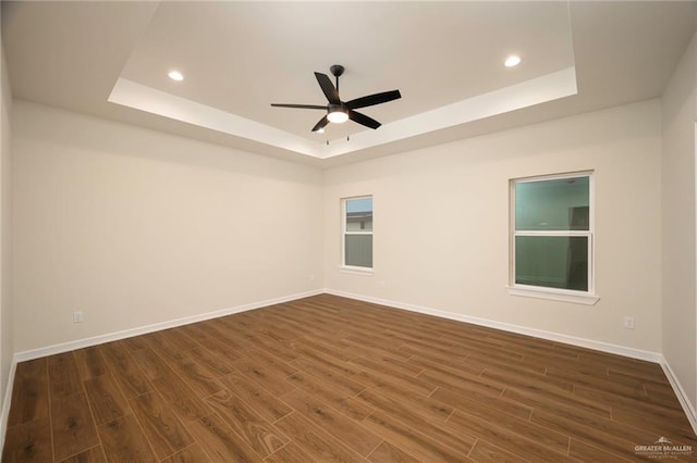 spare room with a raised ceiling, ceiling fan, and dark hardwood / wood-style flooring