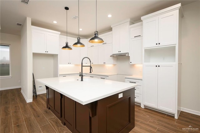 kitchen featuring dark hardwood / wood-style flooring, sink, pendant lighting, white cabinetry, and an island with sink