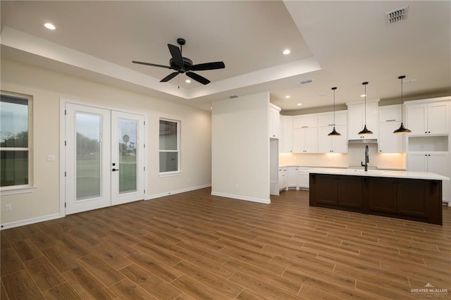 unfurnished living room featuring dark wood-type flooring, french doors, a raised ceiling, sink, and ceiling fan