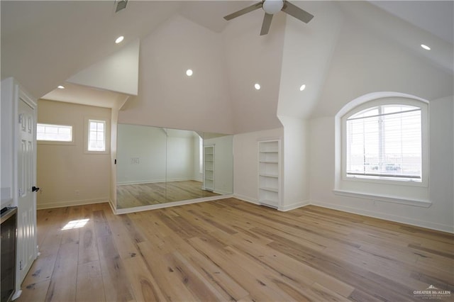 unfurnished living room featuring built in shelves, ceiling fan, high vaulted ceiling, and light wood-type flooring