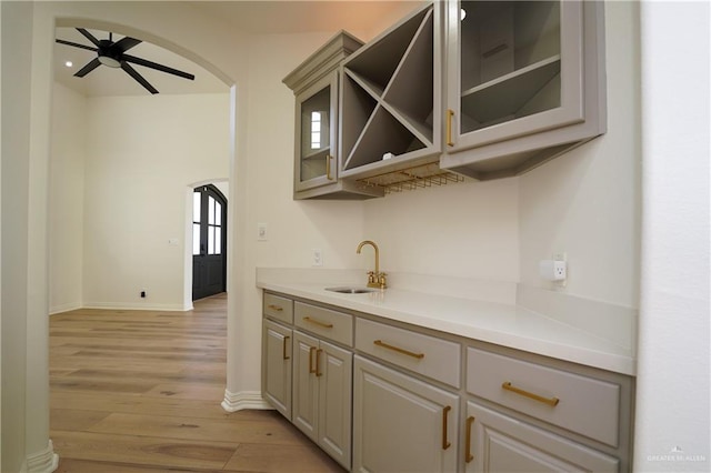 bar featuring gray cabinets, ceiling fan, sink, and light wood-type flooring