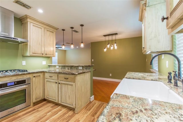 kitchen with wall chimney range hood, sink, appliances with stainless steel finishes, decorative light fixtures, and kitchen peninsula