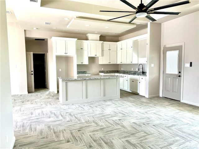 kitchen with white cabinetry, sink, ceiling fan, light stone counters, and a kitchen island