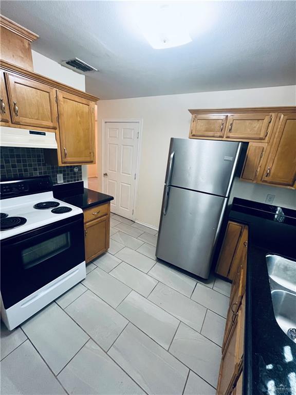 kitchen featuring electric range, visible vents, freestanding refrigerator, under cabinet range hood, and backsplash