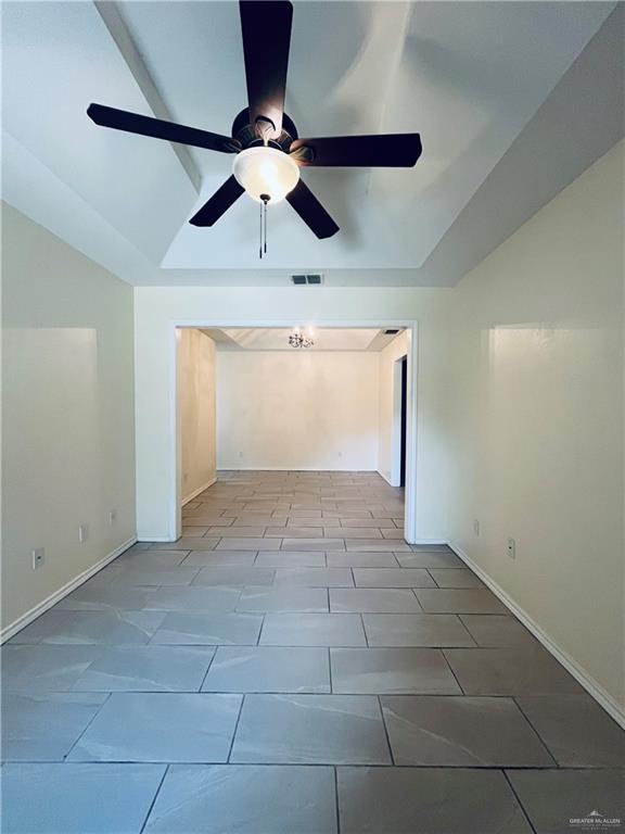 empty room featuring vaulted ceiling, a raised ceiling, and ceiling fan