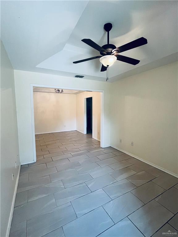 empty room featuring ceiling fan, a tray ceiling, visible vents, and baseboards