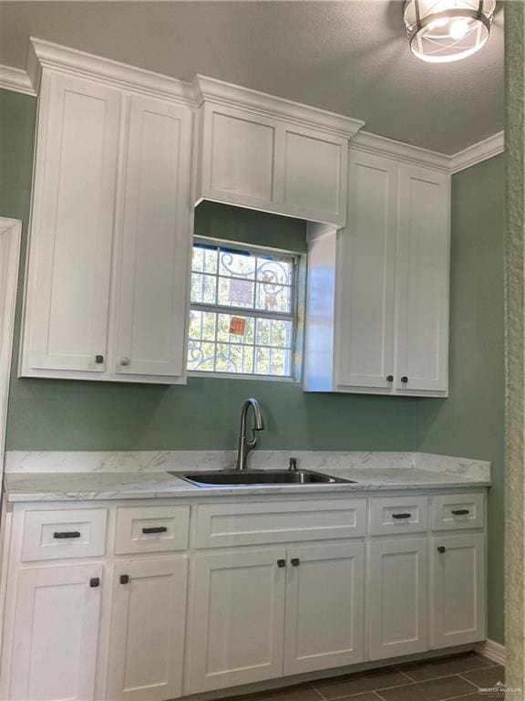 kitchen with white cabinets, light stone counters, dark tile patterned floors, and sink