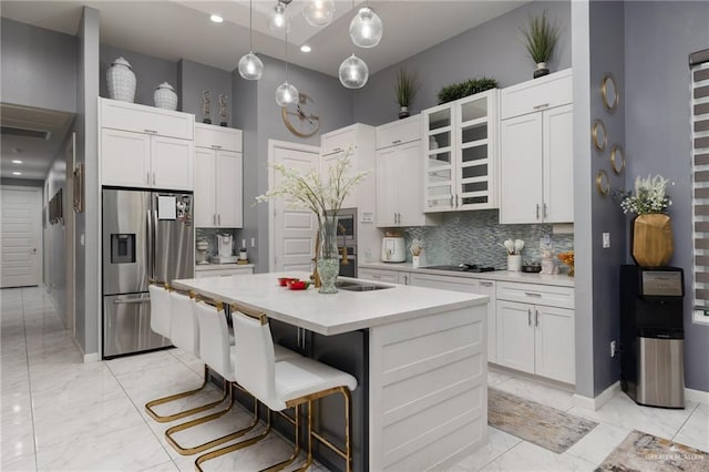 kitchen with a breakfast bar, stainless steel fridge, an island with sink, tasteful backsplash, and decorative light fixtures