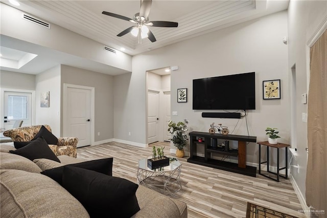 living room with ceiling fan, light wood-type flooring, and a tray ceiling