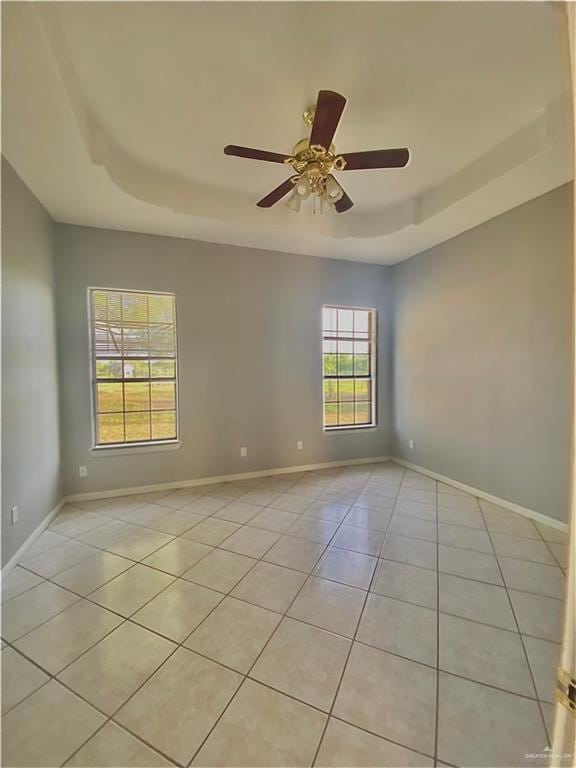 empty room with a raised ceiling, ceiling fan, and light tile patterned flooring