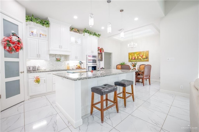 kitchen with light stone counters, a center island, white cabinets, and decorative light fixtures