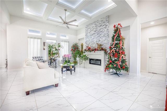 living room with a towering ceiling, coffered ceiling, a large fireplace, ceiling fan, and beamed ceiling