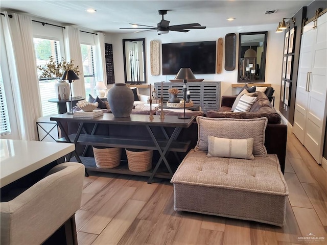 living room featuring a barn door, light hardwood / wood-style flooring, and ceiling fan