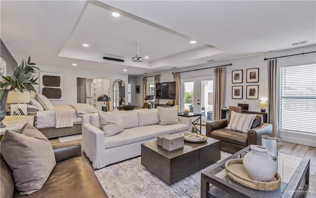 living room with a tray ceiling, a healthy amount of sunlight, and light wood-type flooring