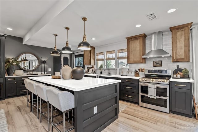 kitchen featuring sink, wall chimney range hood, decorative light fixtures, double oven range, and a kitchen island